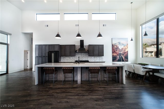 kitchen featuring a breakfast bar area, light countertops, an island with sink, high end black refrigerator, and wall chimney exhaust hood