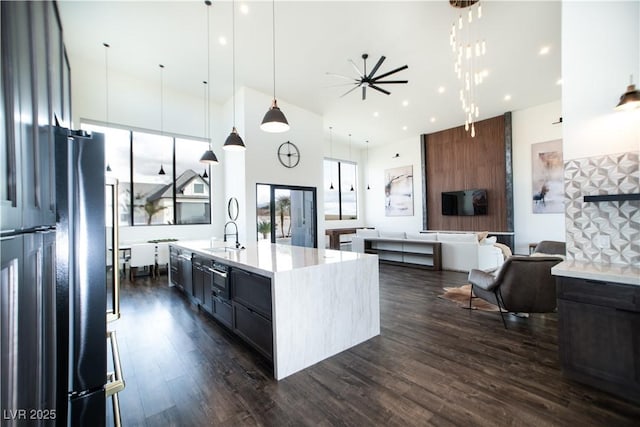 kitchen with dark wood-style floors, open floor plan, a kitchen island with sink, pendant lighting, and a sink