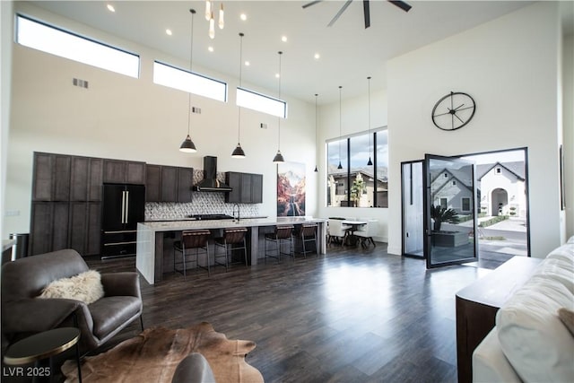 living room with dark wood-style floors, a high ceiling, visible vents, and a ceiling fan