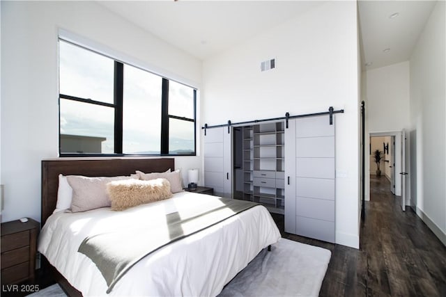 bedroom with high vaulted ceiling, visible vents, dark wood-type flooring, and a barn door