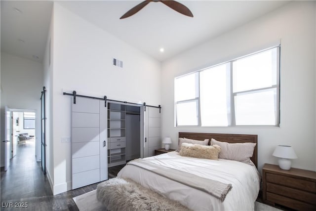 bedroom with a barn door, visible vents, a ceiling fan, dark wood-style flooring, and high vaulted ceiling