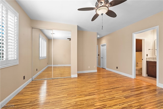 unfurnished bedroom featuring light wood-style flooring, connected bathroom, baseboards, and a ceiling fan