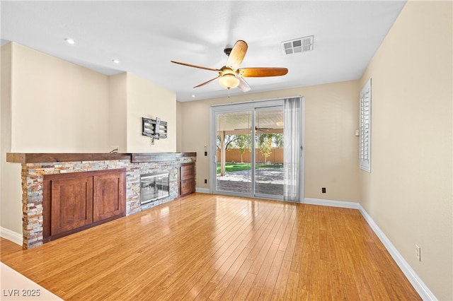 unfurnished living room with a stone fireplace, baseboards, light wood-type flooring, and visible vents