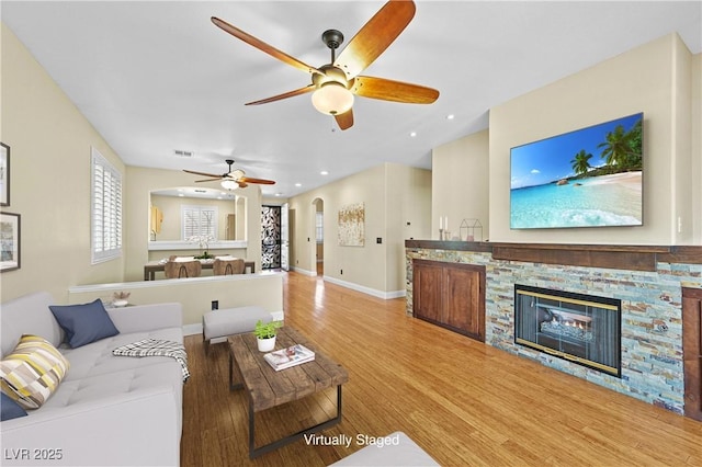 living area with visible vents, wood finished floors, arched walkways, a stone fireplace, and baseboards