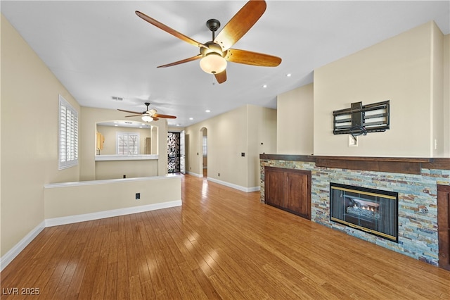 unfurnished living room with arched walkways, a fireplace, baseboards, and hardwood / wood-style floors