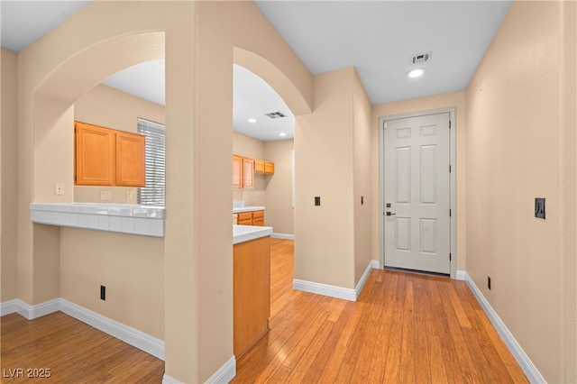 corridor featuring arched walkways, light wood-style floors, visible vents, and baseboards