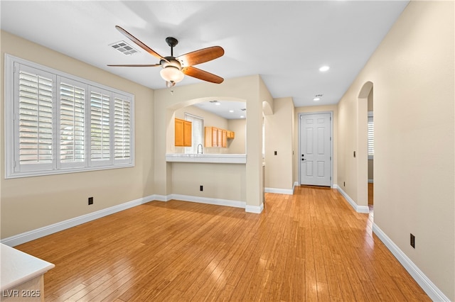 unfurnished living room featuring a ceiling fan, baseboards, visible vents, arched walkways, and light wood-style floors