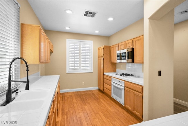 kitchen featuring white appliances, light wood-type flooring, visible vents, and a sink