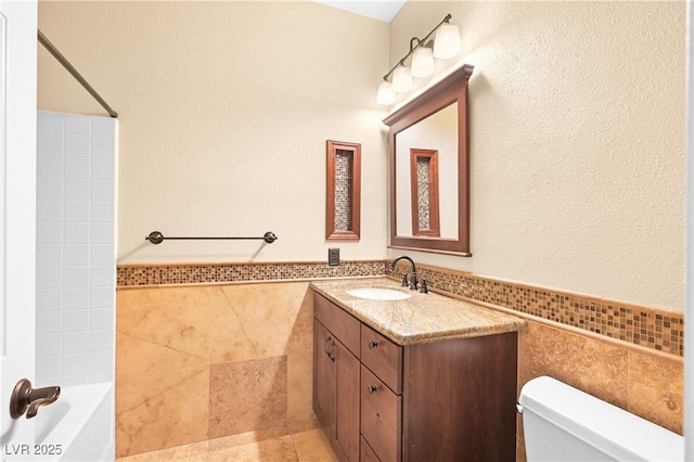 full bath with toilet, tile walls, wainscoting, bathtub / shower combination, and vanity