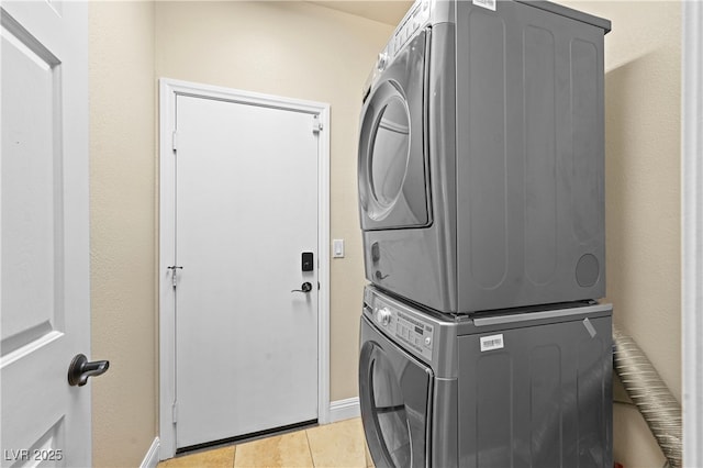 clothes washing area featuring baseboards, stacked washer and clothes dryer, light tile patterned flooring, and laundry area