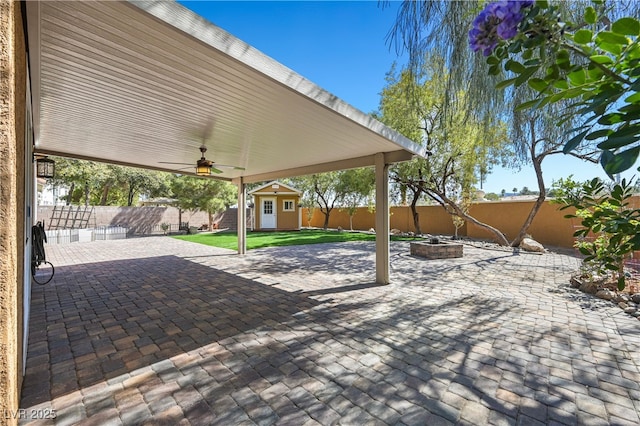 view of patio with a ceiling fan, an outdoor structure, a fenced backyard, and an outdoor fire pit