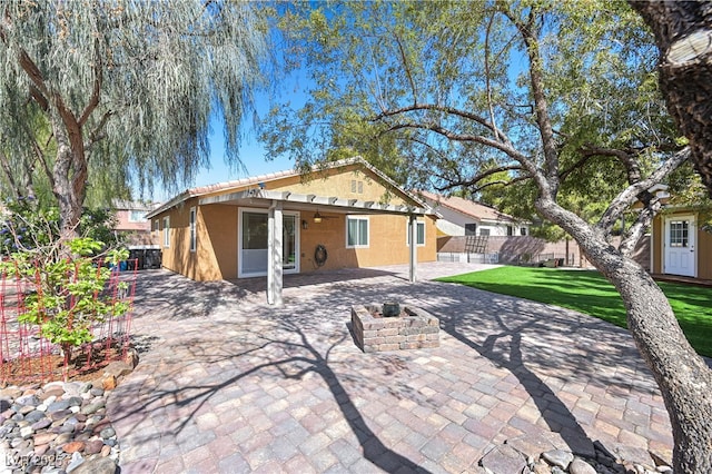 rear view of house with fence, an outdoor fire pit, stucco siding, a lawn, and a patio area