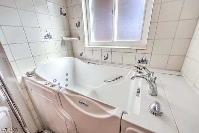 bathroom featuring a tub with jets and tile walls