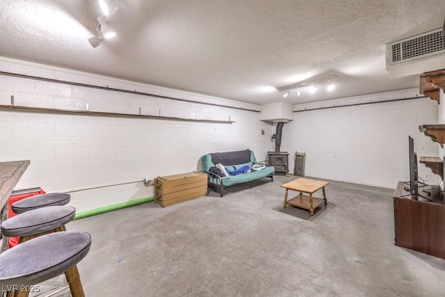 finished basement featuring visible vents, a textured ceiling, a wood stove, and concrete block wall