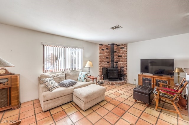 living room featuring a wood stove, visible vents, a textured ceiling, and light tile patterned floors