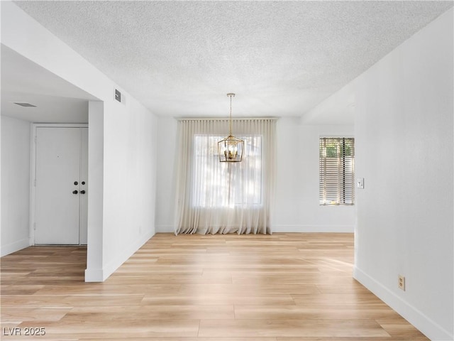 unfurnished dining area with a notable chandelier, visible vents, a textured ceiling, light wood-type flooring, and baseboards