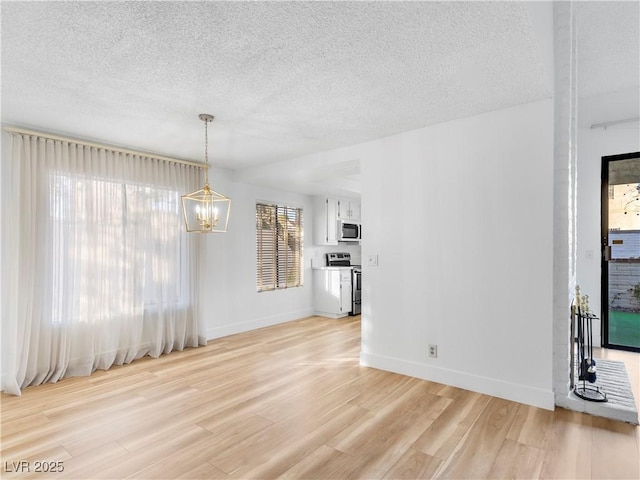 unfurnished dining area featuring light wood-style floors, a chandelier, a textured ceiling, and baseboards