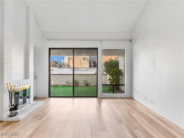 unfurnished room with a brick fireplace, baseboards, and wood finished floors