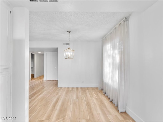 unfurnished room featuring light wood finished floors, visible vents, baseboards, a textured ceiling, and a notable chandelier