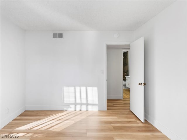 unfurnished room featuring light wood-style floors, visible vents, a textured ceiling, and baseboards