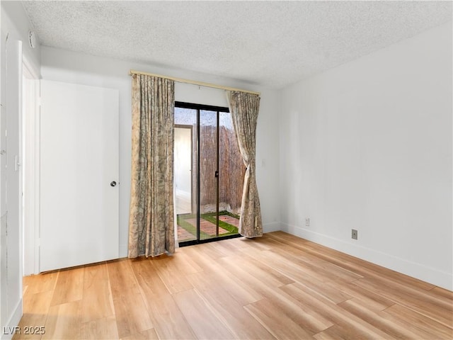 empty room with a textured ceiling, light wood-type flooring, and baseboards