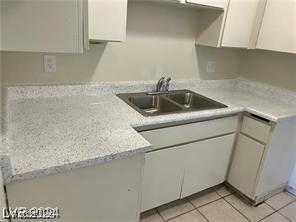 kitchen featuring light stone countertops, white cabinets, a sink, and light tile patterned flooring