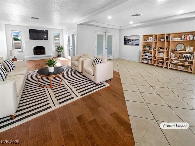 living area featuring visible vents, french doors, a fireplace with raised hearth, and light wood-style flooring