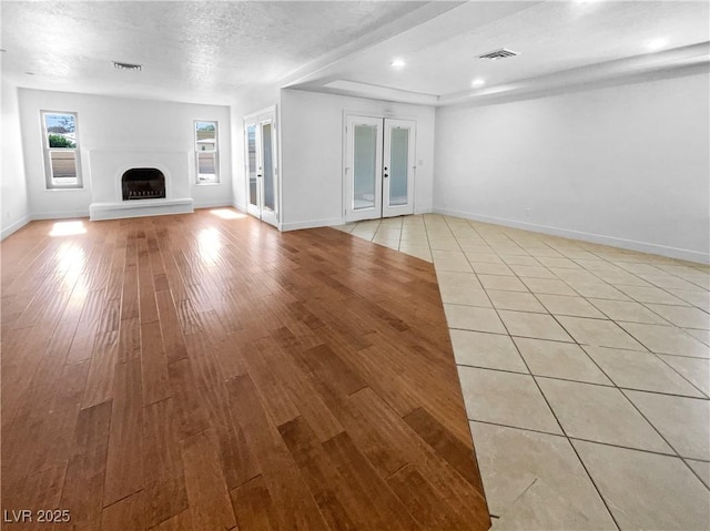 unfurnished living room featuring light wood-style flooring, visible vents, a fireplace with raised hearth, and baseboards