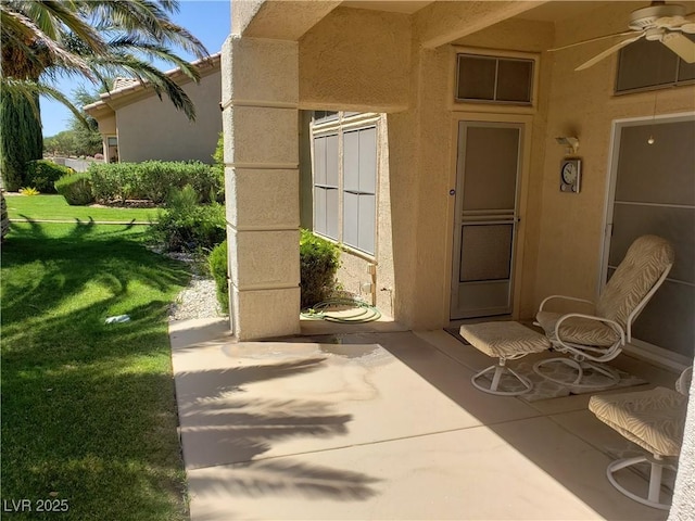 property entrance with a patio, a lawn, a ceiling fan, and stucco siding