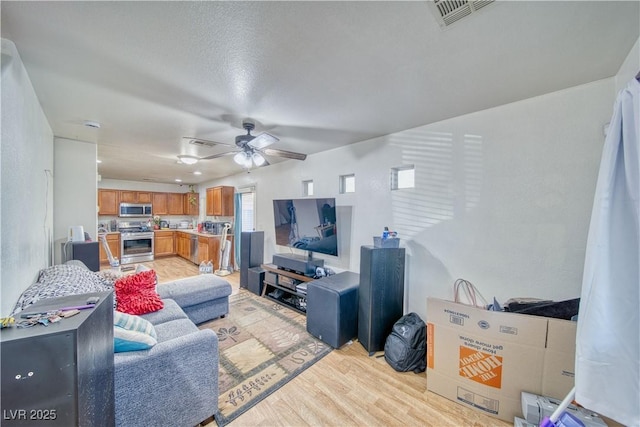 living room with visible vents, light wood-type flooring, and a ceiling fan