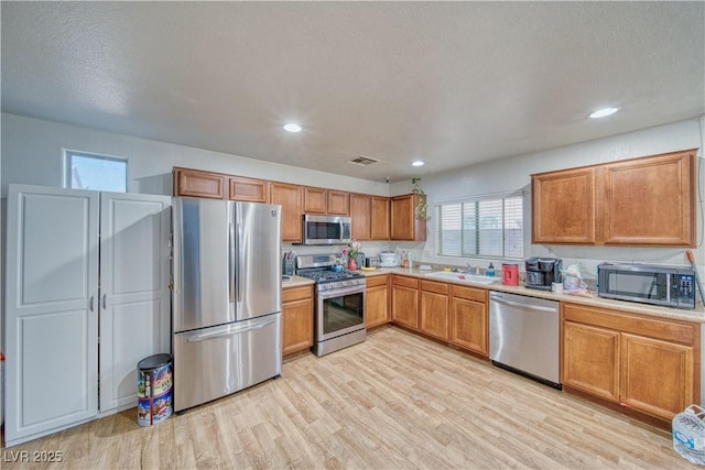 kitchen featuring light countertops, light wood-style flooring, brown cabinetry, and appliances with stainless steel finishes