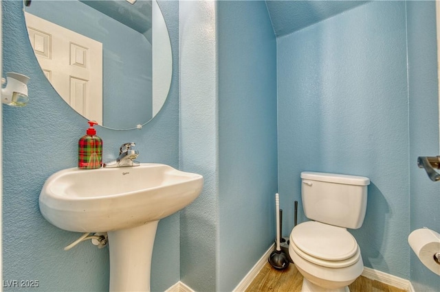 bathroom with baseboards, toilet, wood finished floors, and a textured wall