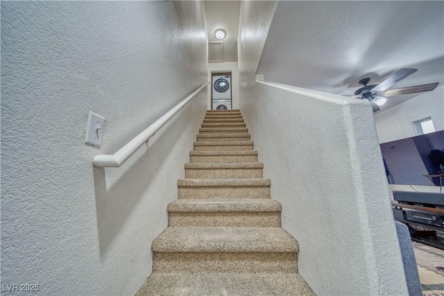 stairway with a ceiling fan and a textured wall