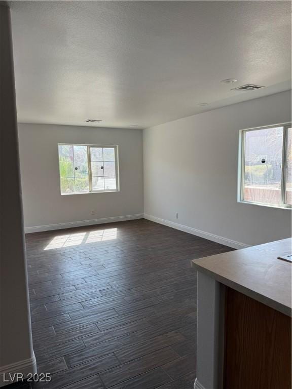 unfurnished room with dark wood-type flooring, visible vents, and baseboards