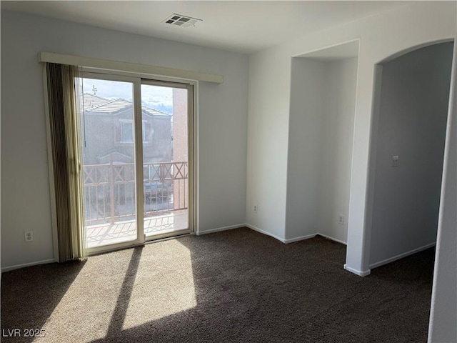 empty room featuring arched walkways, visible vents, dark carpet, and baseboards