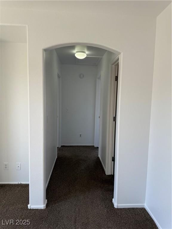 corridor featuring baseboards, dark carpet, and arched walkways