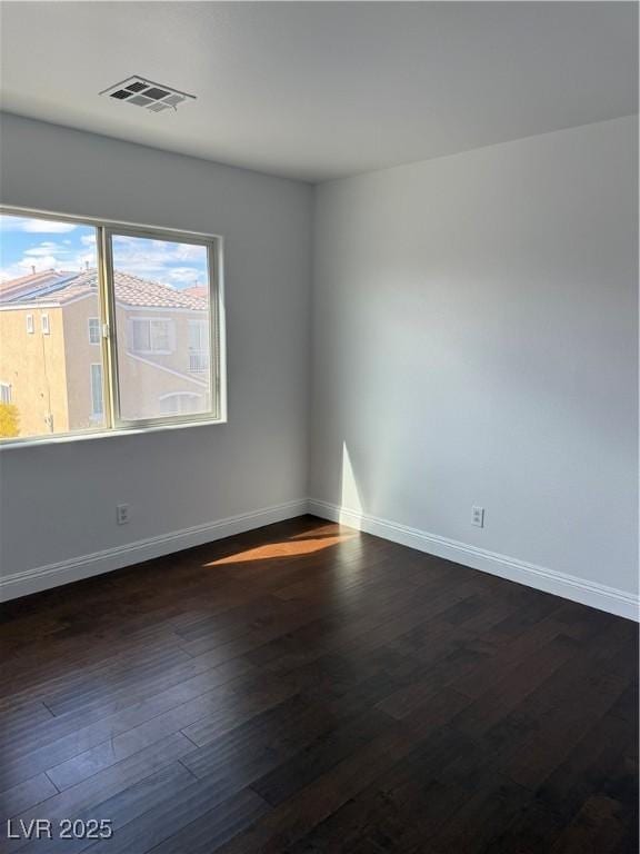 unfurnished room with visible vents, dark wood finished floors, and baseboards