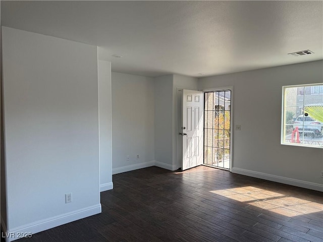 empty room with visible vents, dark wood finished floors, and baseboards