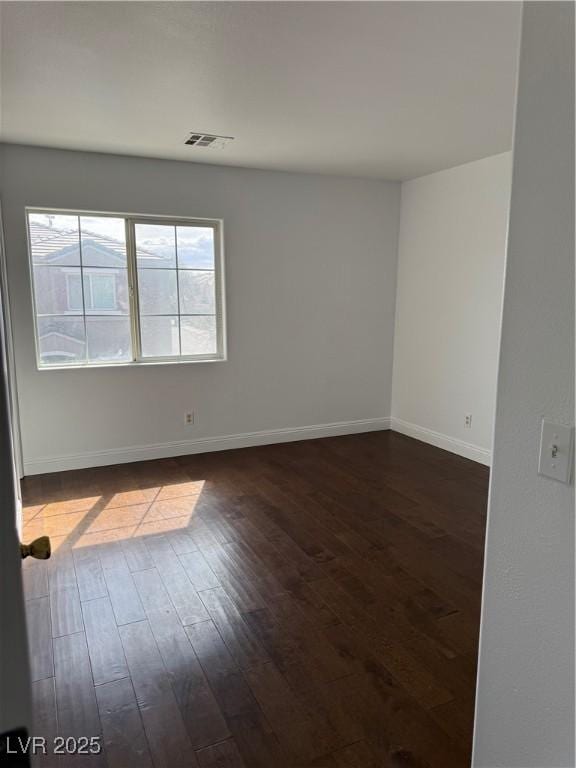 empty room with dark wood-type flooring, visible vents, and baseboards