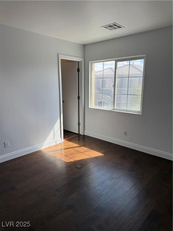 empty room with dark wood-style floors, visible vents, and baseboards