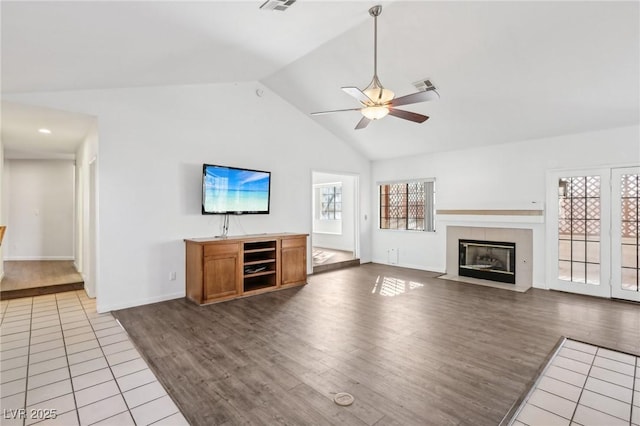 unfurnished living room with visible vents, a tiled fireplace, vaulted ceiling, ceiling fan, and wood finished floors