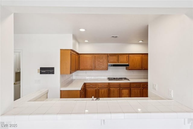 kitchen with stainless steel gas cooktop, recessed lighting, visible vents, brown cabinetry, and under cabinet range hood