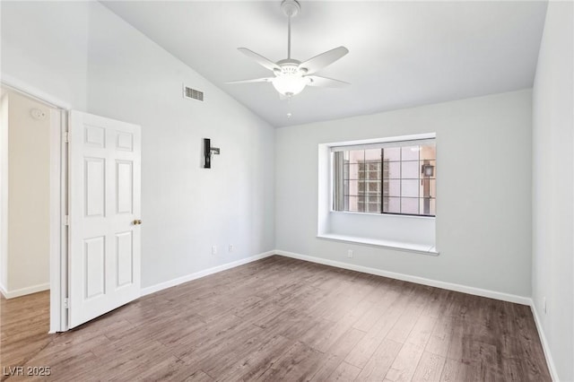 spare room with wood finished floors, visible vents, baseboards, vaulted ceiling, and a ceiling fan