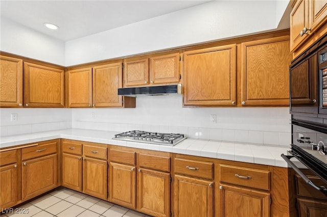 kitchen featuring light tile patterned floors, brown cabinetry, under cabinet range hood, black appliances, and recessed lighting