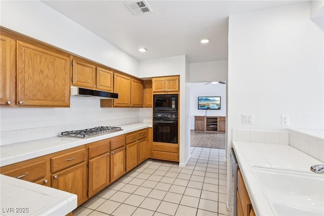 kitchen featuring tile counters, visible vents, under cabinet range hood, and black appliances