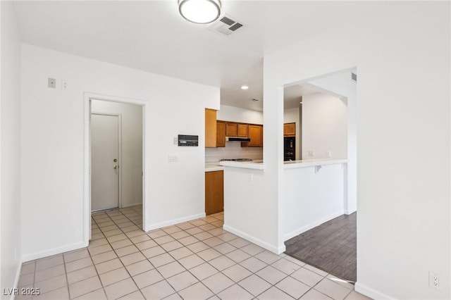 kitchen with under cabinet range hood, a peninsula, visible vents, light countertops, and brown cabinetry