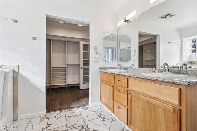 bathroom with marble finish floor, a spacious closet, visible vents, and a sink