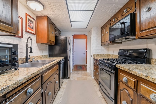 kitchen featuring black appliances, backsplash, a sink, and stone tile floors