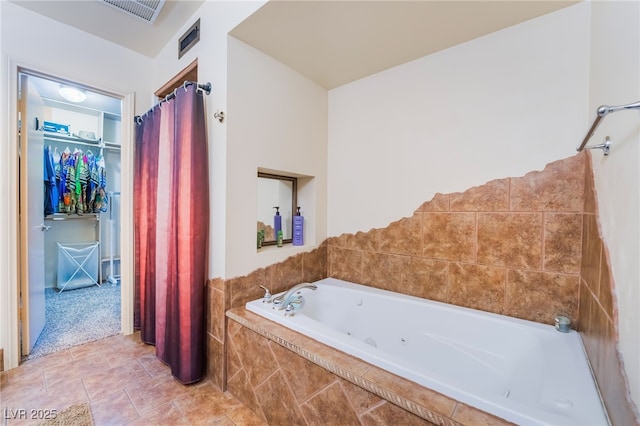 bathroom with a garden tub, a walk in closet, visible vents, and tile patterned floors