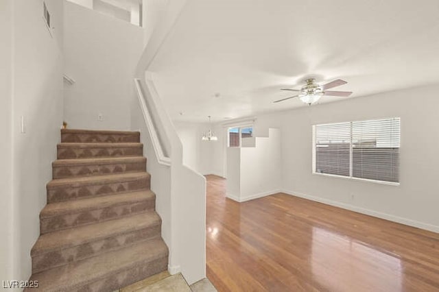 stairs featuring visible vents, baseboards, wood finished floors, and ceiling fan with notable chandelier